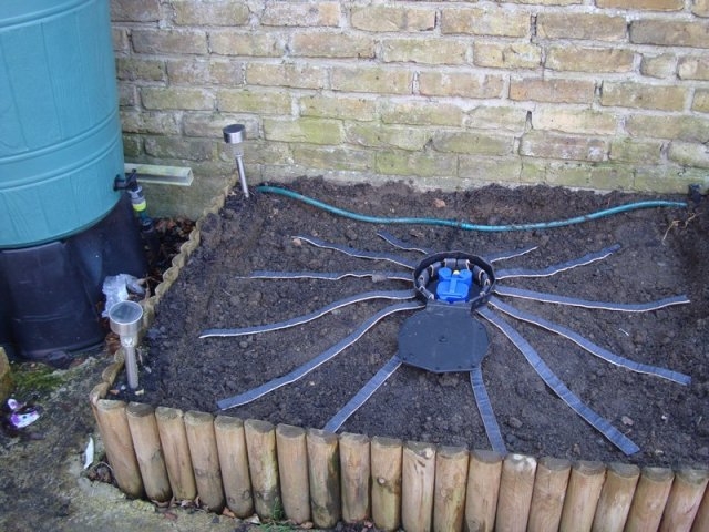 AQUAbox Spyder sistema de irrigação por gotejamento em canteiro com madeira e tambor azul ao lado