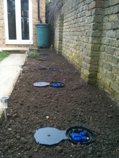 AQUAbox Spyder Vários registos de água no solo entre parede de tijolos e passeio de pedra