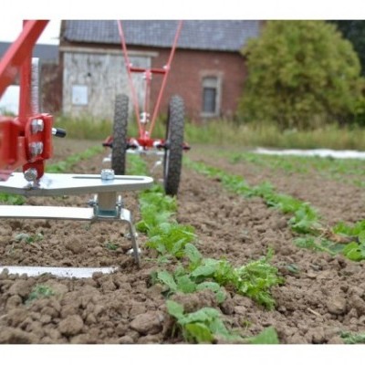Implemento agrícola vermelho com lâminas circulares e rodas em terreno arado com plantas verdes