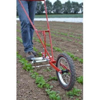 Carrinho agrícola manual vermelho com roda grande em horta com plantas verdes