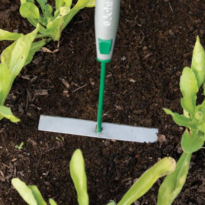 Rastelo pequeno de jardinagem com lâmina metálica em terra entre plantas verdes
