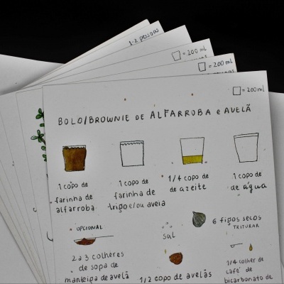 Folha com receita ilustrada de bolo/brownie de alfarroba e avelã com ingredientes e quantidades em português