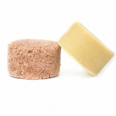 Dois champôs sólidos, um bege liso e outro castanho granuloso sobre fundo branco.