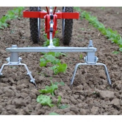 Cultivador de linha metálico em terreno arado com plantas verdes