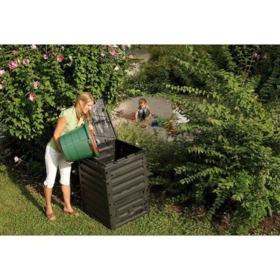 Contentor preto para compostagem em jardim com mulher a colocar material orgânico