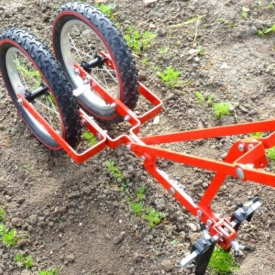 Acessório agrícola metálico vermelho com duas rodas de borracha pretas em solo de terra