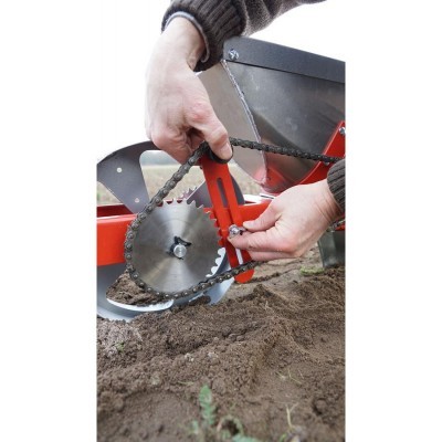 Implemento agrícola com corrente metálica e roda dentada junto de solo de terra arada