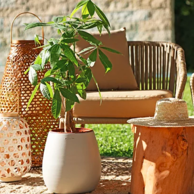 Móveis de exterior com poltronas castanho claro, mesa em madeira, chapéu de palha e vasos decorativos num jardim