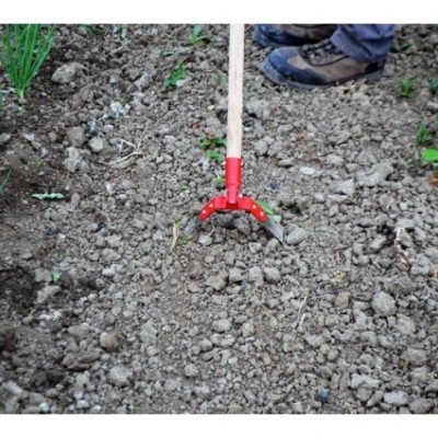 Enxada manual com cabo de madeira e cabeça vermelha em terra solta num jardim.