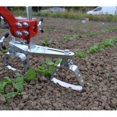 Ferramenta agrícola metálica vermelha e prateada em solo com plantas verdes