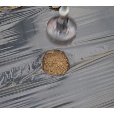 Lámina plástica preta no solo com buraco e objeto metálico acima