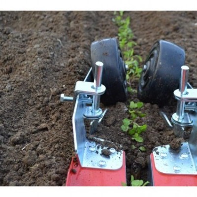 Rodas metálicas com pneus pretos e suportes vermelhos em solo fértil com plantas verdes