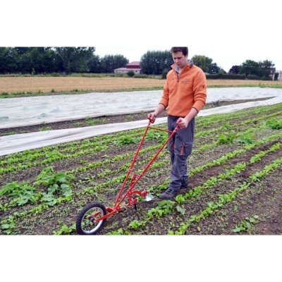 Homem trabalhando numa horta com ferramenta agrícola vermelha e roda preta.