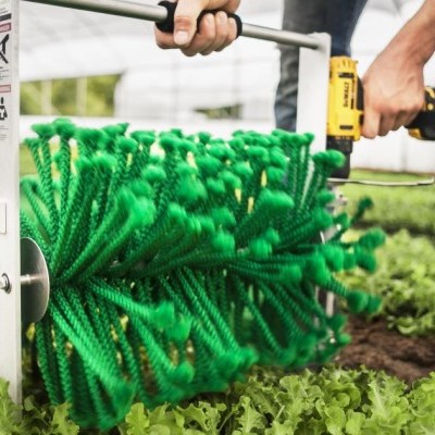 Escova verde com cerdas grossas em estufa, operada por pessoa de calças e sapatos castanhos