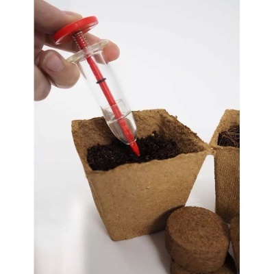 Vaso biodegradável com terra e ferramenta vermelha para plantar semente