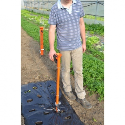 Pessoa usando haste laranja com alavanca para fazer furos em plástico no solo para plantação