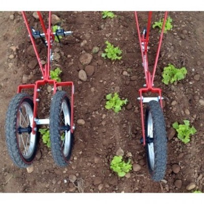 Dispositivos agrícolas vermelhos com rodas pretas sobre solo com plantas verdes.