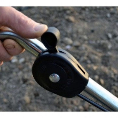 Mão a segurar peça metálica com mecanismo preto e texto em relevo, fundo de terra com pedras