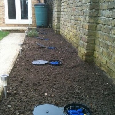 Vários registos de água no solo entre parede de tijolos e passeio de pedra