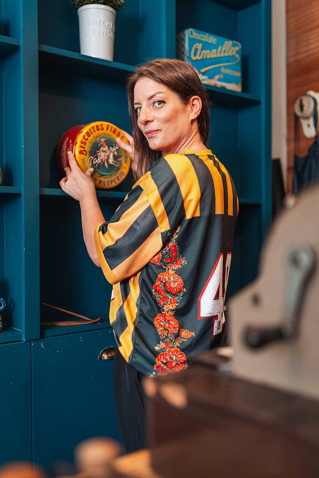 Camisola de Jogo Retro - Edição Amarelo & Preto Mulher segurando lata redonda de metal em armário azul
