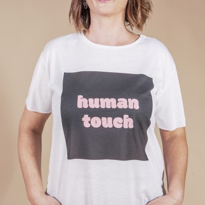 Mulher a usar t-shirt branca com impressão 'human touch' em preto e rosa e jeans pretos.
