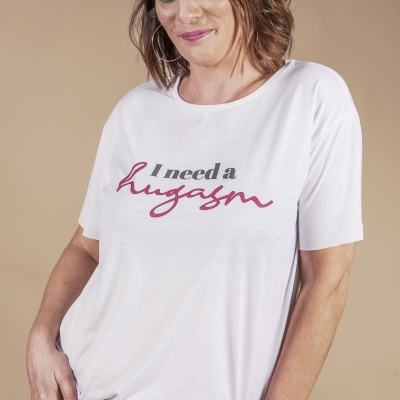 Mulher com t-shirt branca com texto 'I need a hugasm' e calças de ganga rasgadas