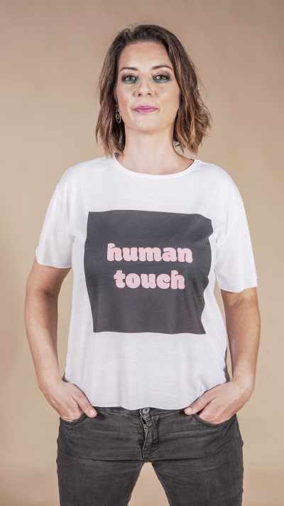 Mulher a usar t-shirt branca com impressão 'human touch' em preto e rosa e jeans pretos.