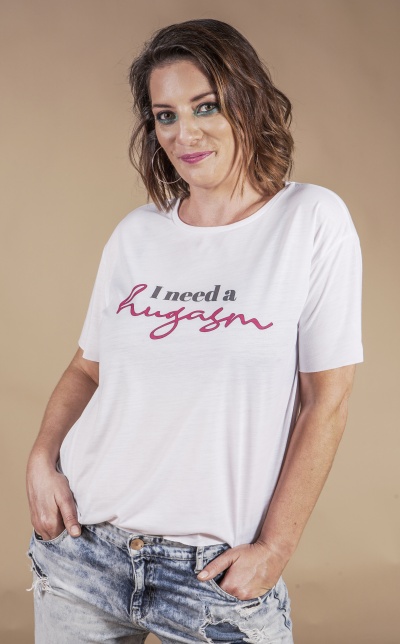 Mulher com t-shirt branca com texto 'I need a hugasm' e calças de ganga rasgadas