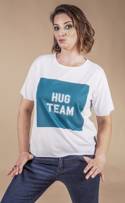 T-shirt branca com estampa azul e texto HUG TEAM, usada com calças de ganga num fundo bege.