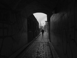 East Ending, Eduardo Brito Rua estreita de pedra e figura ao longe sob um arco em preto e branco