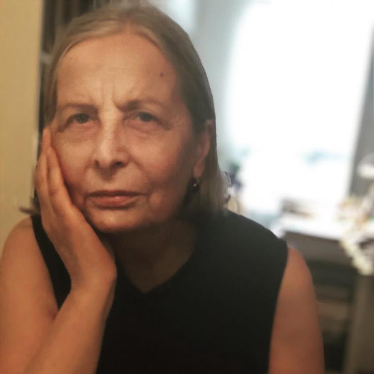 Mulher com blusa preta sem mangas e cabelo grisalho apoiando a face