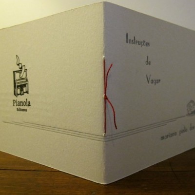 Caixa branca com texto e ilustrações em papel/cartão, costura vermelha visível.