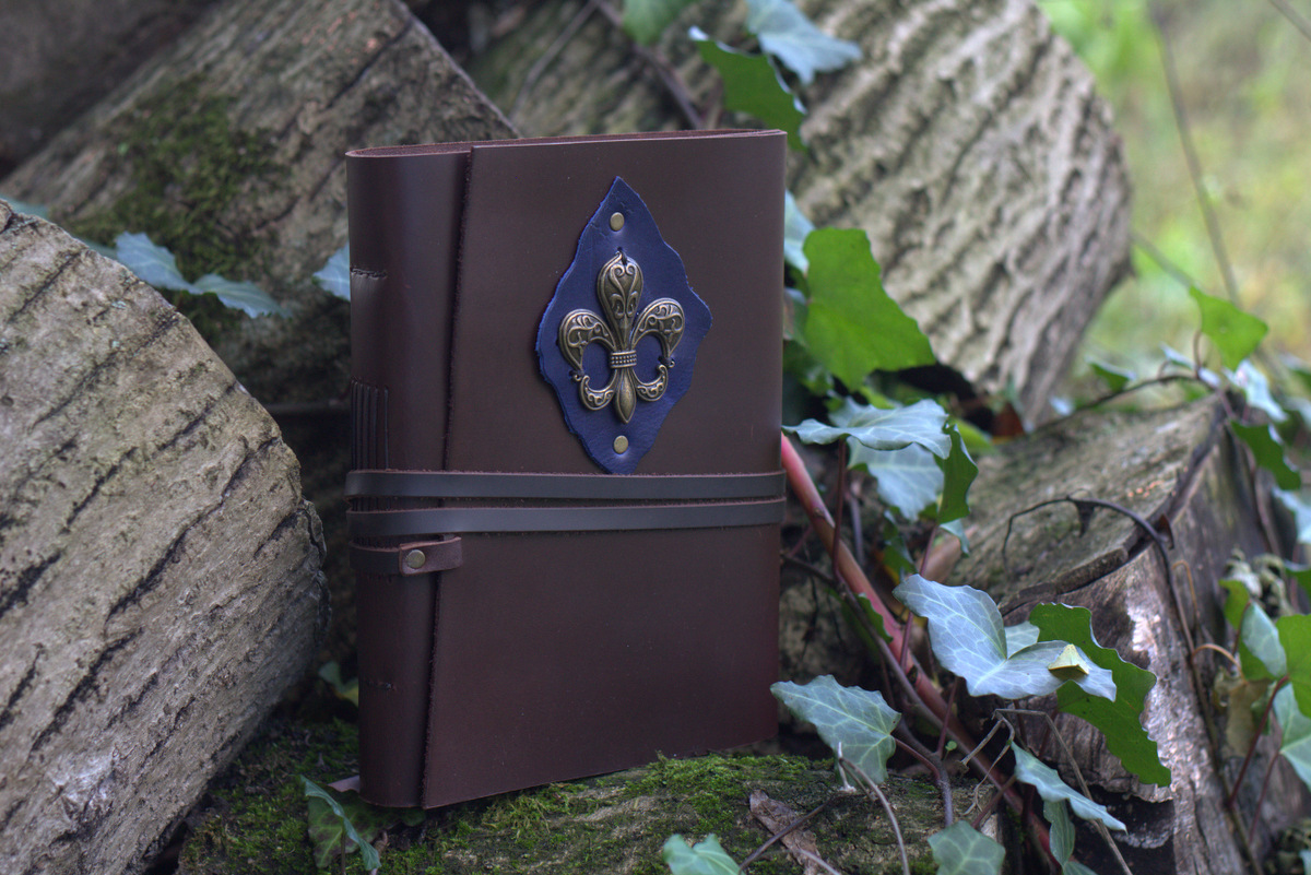 Caderno Flor-de-lis Caderno de capa dura em couro castanho com decoração metálica azul e prata, sobre troncos e musgo