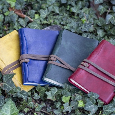 Cadernos de capa em couro coloridos com fita de amarração sobre folhas verdes