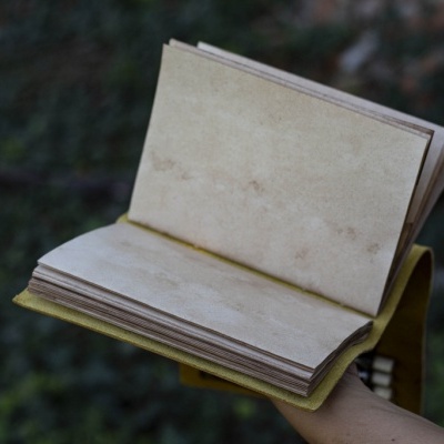 Caderno antigo com capas amarelas e páginas manchadas segurado à mão