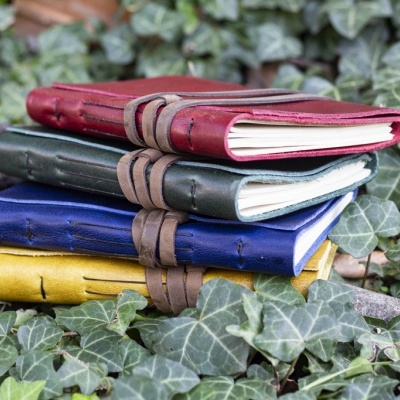 Quatro cadernos de couro coloridos empilhados sobre folhas verdes
