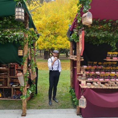 Dois stands de venda ao ar livre com decoração natural e um homem vestido vintage a fumar um cachimbo entre eles