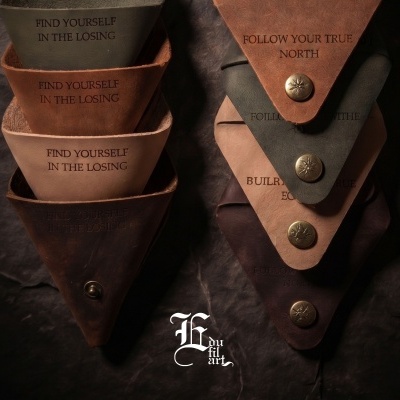 Porta-moedas triangulares de pele com textos em inglês e fechos metálicos gravados.