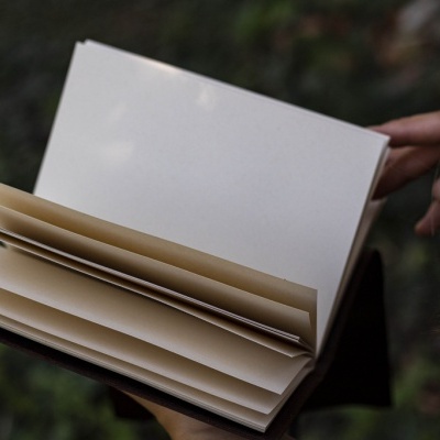 Livro ou caderno aberto com páginas em branco e capa preta segurado por mãos