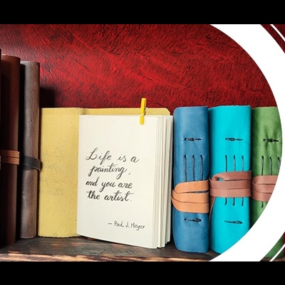 Cadernos de couro coloridos com cadernos fechados por tiras e um aberto com citação manuscrita