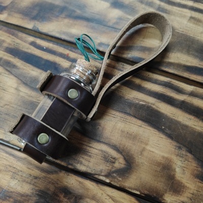 frasco de vidro com tampa de cortiça preso a alça de couro sobre madeira