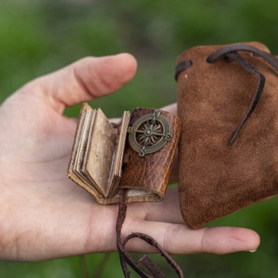 Mão a segurar mini livro de couro castanho e saco de veludo castanho com cordão