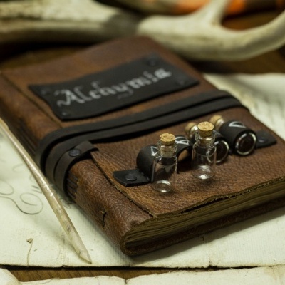 Caderno em pele castanha com fecho e pequenos frascos, com penas e papel escrito à mão