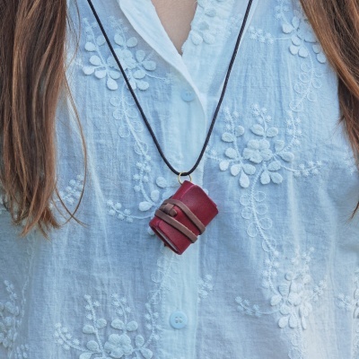 Colar com pequeno livro em couro vermelho pendurado em camisa branca bordada