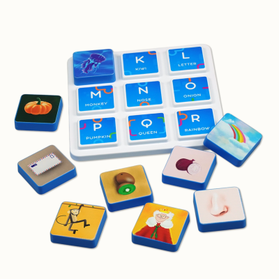 Blue square tiles with letters and words in a white tray, with scattered illustrated tiles including a pumpkin, rainbow, monkey, queen, nose, envelope, and kiwi.