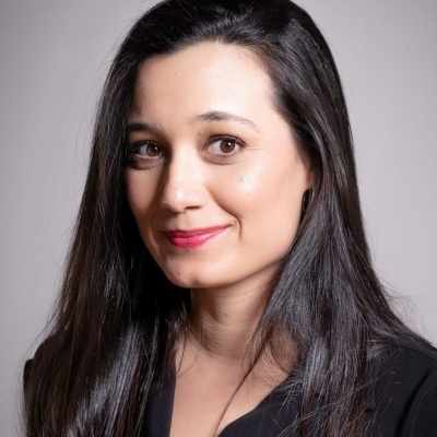 Mulher com cabelo comprido castanho escuro e roupa preta sobre fundo cinzento