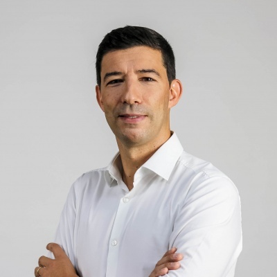 Homem de camisa branca com braços cruzados sobre fundo cinzento