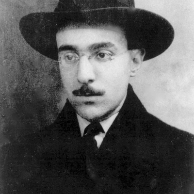 Homem com chapéu escuro, óculos e casaco preto numa fotografia a preto e branco