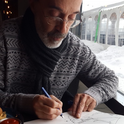 Homem a desenhar numa mesa junto à janela com neve do lado de fora