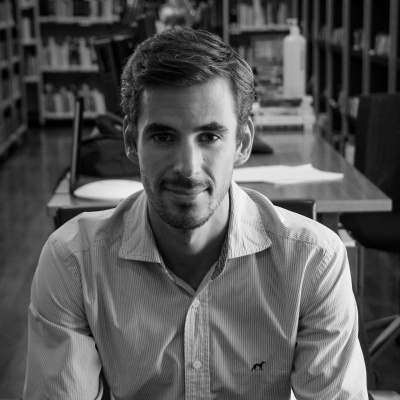 Homem jovem com camisa em ambiente com livros e mesas